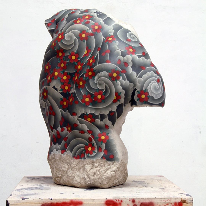 Italian artist's sculpture with floral tattoo design, featuring red flowers and swirling patterns on a stone surface.