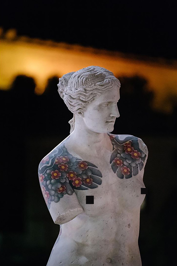 Sculpture with vibrant tattoos on shoulders and chest by Italian artist, showcasing tattoos beyond human skin.