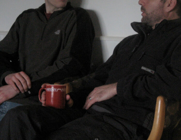 Two men sitting closely, one holding a red mug, illustrating specific little things that are irritating to people.
