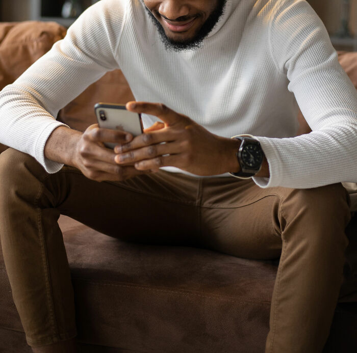 Man in casual outfit sitting on couch, smiling while using smartphone, highlighting specific little things irritating people.