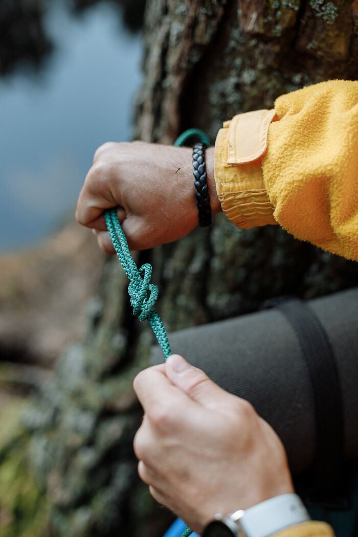 Person's hands tying a knot in a rope outdoors near a tree, illustrating specific little things that are irritating.