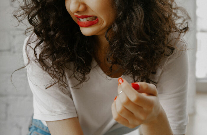 Woman with curly hair and red lipstick grimacing in irritation, illustrating specific little things that are irritating.