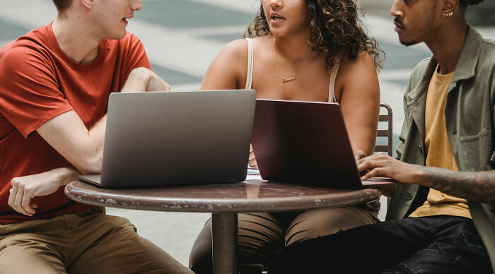 Three people sitting at a round table with laptops, discussing specific little things that are so irritating to people.