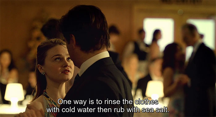 Woman and man talking at a formal event with subtitle about rinsing clothes with cold water and sea salt irritation tip.