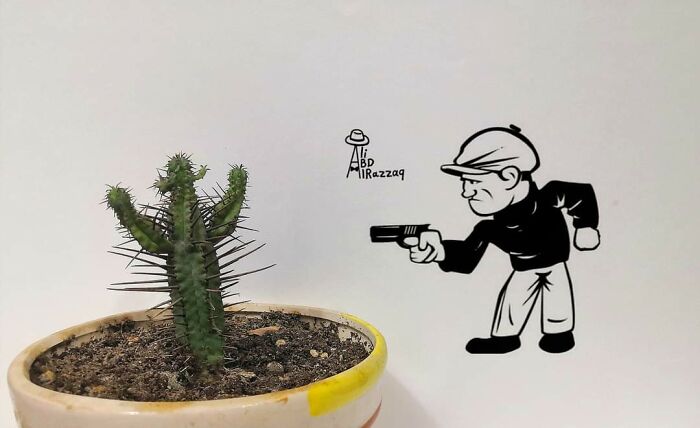 Cactus plant in a pot with an interactive illustration of a man aiming a gun at the cactus as part of creative artwork.