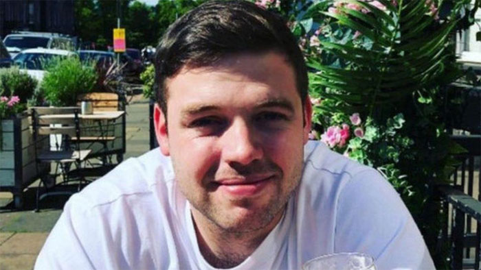 Young man sitting outdoors at café, smiling on a sunny day, illustrating really cool and interesting facts from online community.