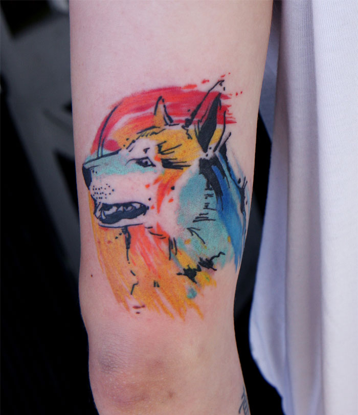 Vibrant watercolor wolf tattoo on arm, showcasing artistry and creativity from an experienced tattoo artist.