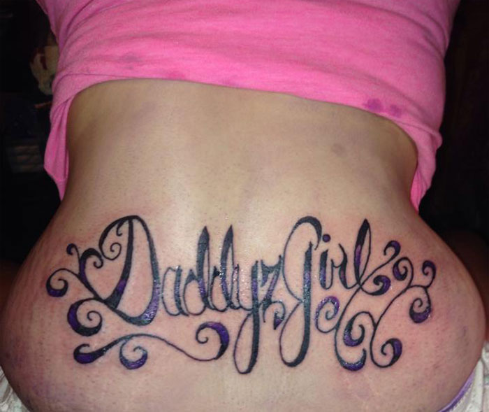Lower back "Daddy's Girl" tattoo in cursive script, with swirls, showing a tattoo virgin's challenging choice.