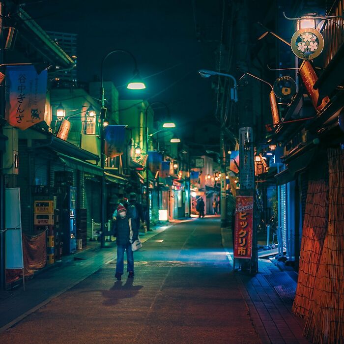 Night street scene in Japan with illuminated signs and a person walking, capturing the beauty of Japan’s urban charm.