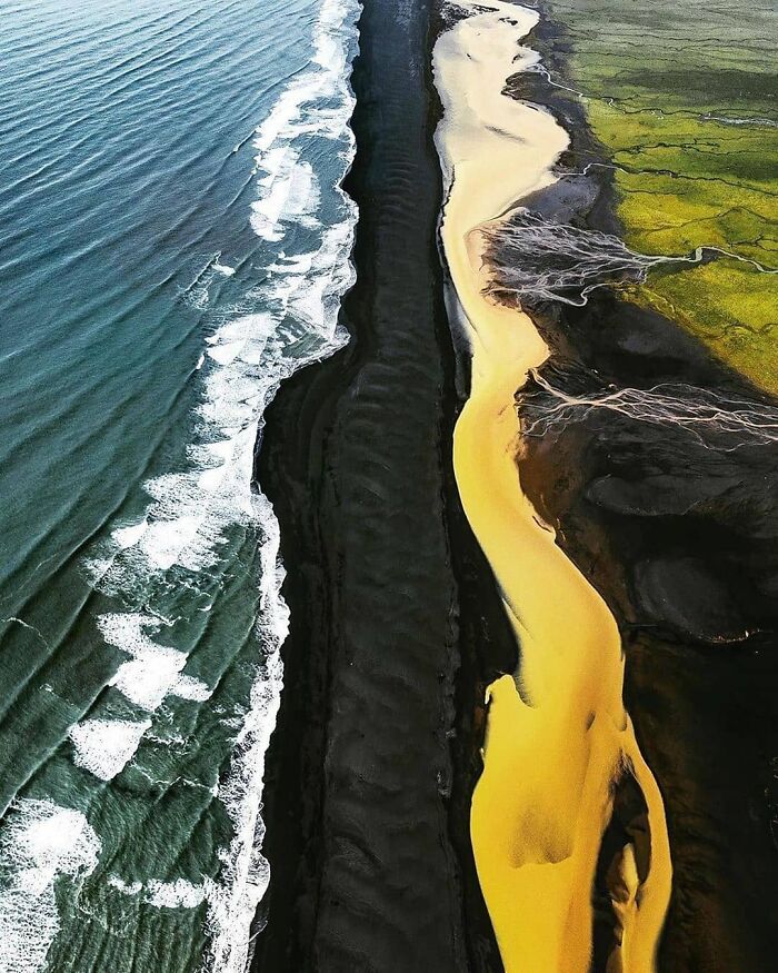 En esta bellísima fotografía se puede ver cómo el mar azul, la playa de arena negra, el río amarillo y los campos verdes convergen en perfecta armonía