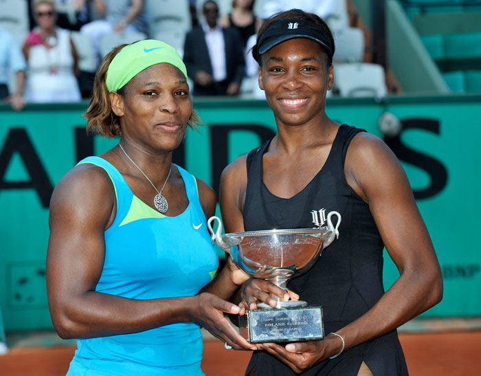 Venus and Serena Williams standing next to each other, smiling and holding a trophy
