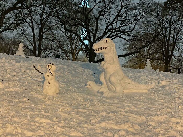 This T-Rex Chasing A Snowman Snow Sculpture