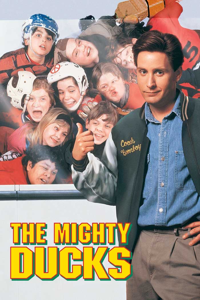 Coach with hockey team in '90s kids movie, "The Mighty Ducks," posing in front of excited young players.