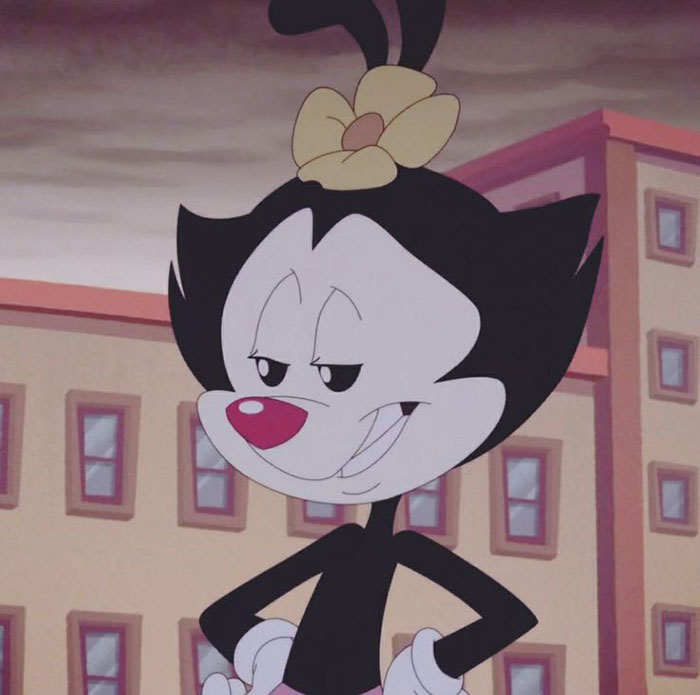Cute animated character with a flower on their head, smiling confidently against a building backdrop.
