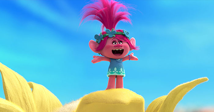 Cute animated character with pink hair and a blue dress, standing joyfully on a yellow surface against a clear sky.