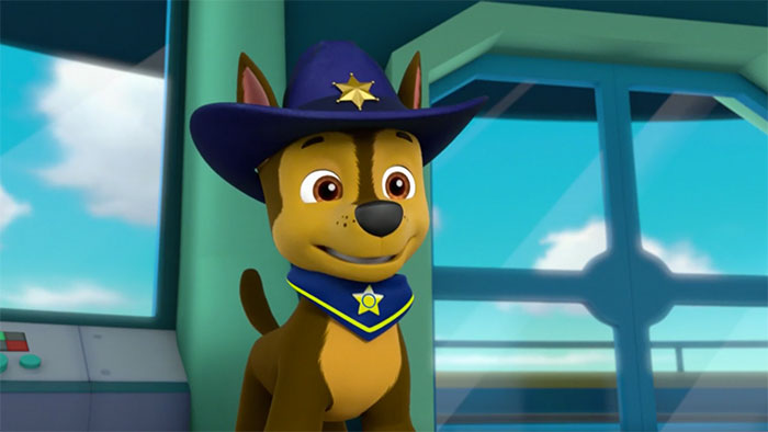 Cute animated character dog wearing a blue hat and star badge, standing indoors with a cheerful expression.