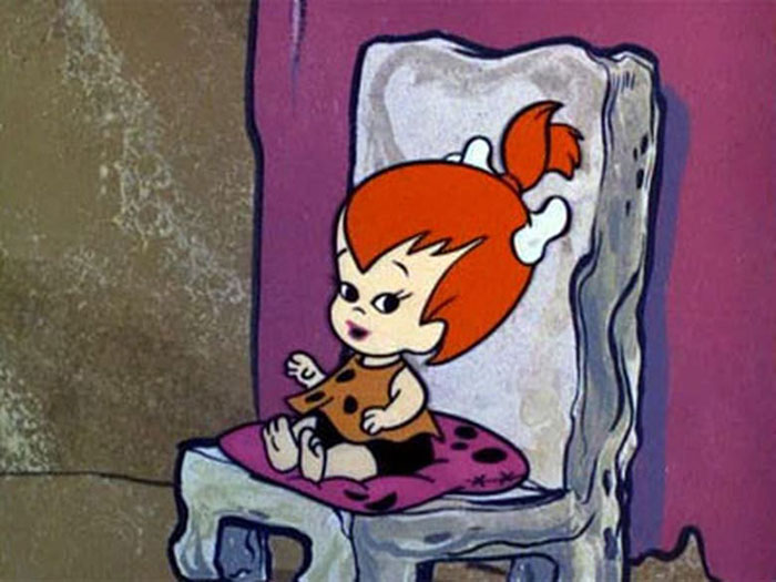 Cute animated character with red hair and bone accessory sitting on a colorful chair.