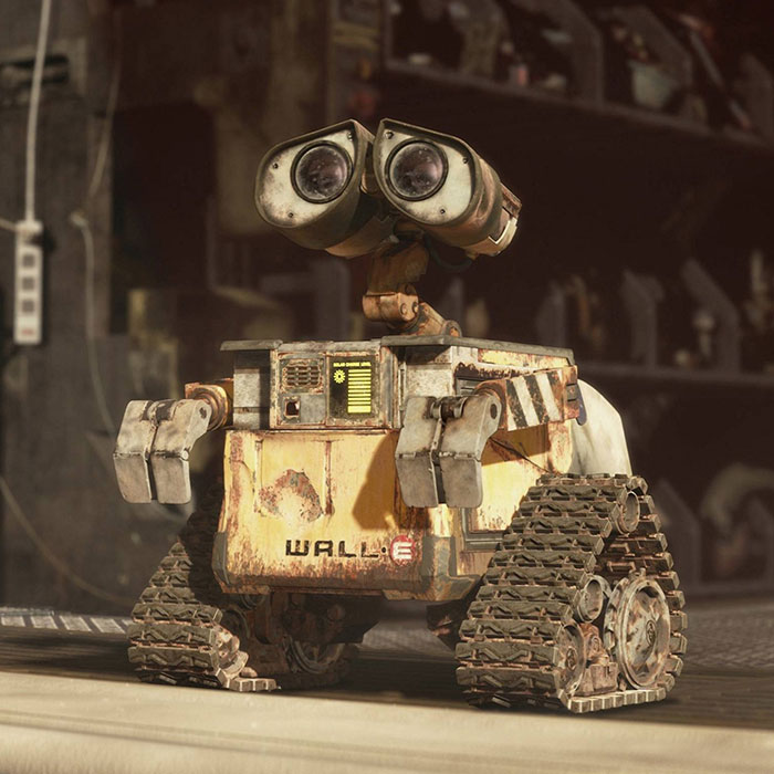 Cute animated robot character with binocular eyes, rusted yellow body, and tank-like treads in a workshop setting.