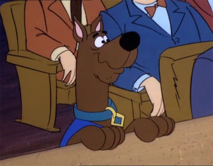 Cute animated character sitting in a courtroom, surrounded by people in suits.