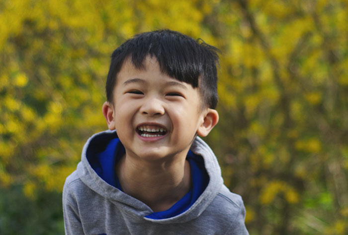 A boy in gray hoodie standing near yellow leaf trees and smiling