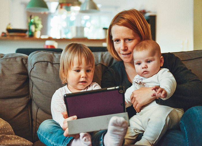 two babies and woman sitting on sofa while watching tablet