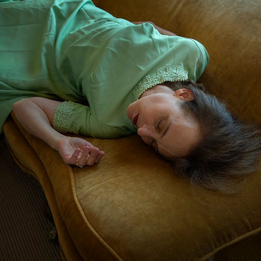 Woman in a vintage green dress lying on a brown couch, captured by photographers showcasing beautiful women worldwide.