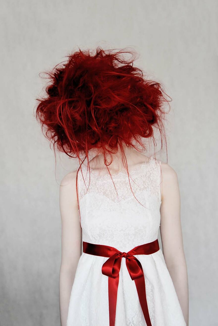 Woman with bright red hair in a white lace dress with a red ribbon, captured by photographers highlighting beautiful women around the world.