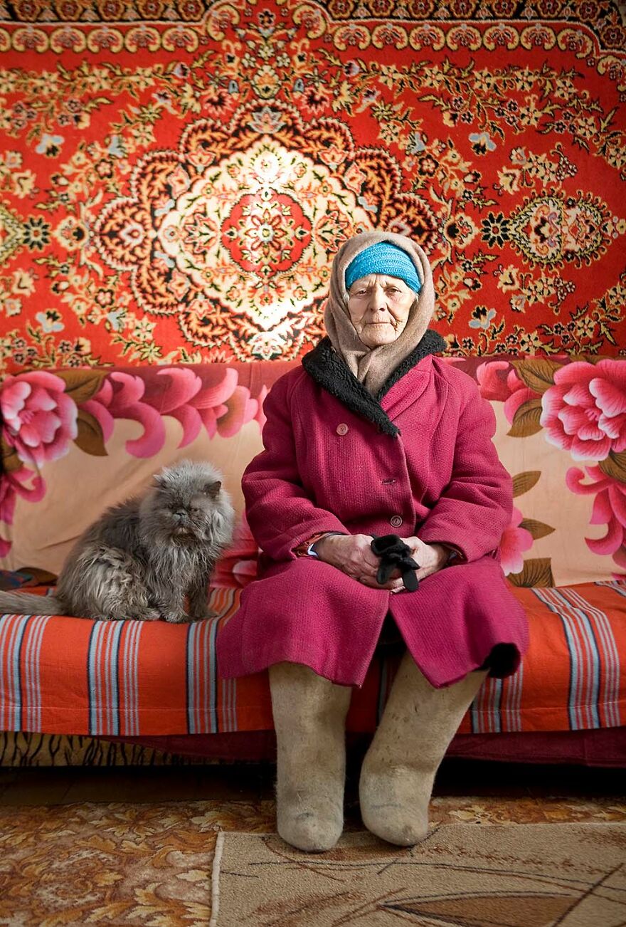Elderly woman sitting on a colorful couch with her fluffy cat, captured by photographers showcasing beautiful women worldwide.