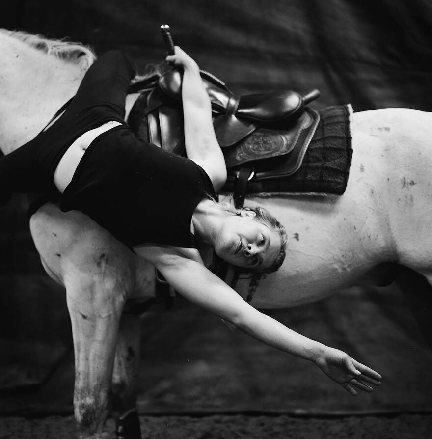Woman captured by photographers lying backward on a white horse, showcasing beauty and grace in a striking black and white image.