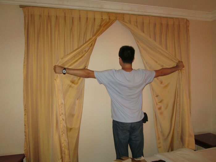 Hombre abriendo las cortinas de su habitación de hotel sin ventanas