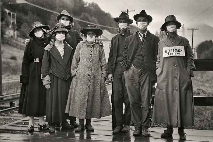 Viajeros de tren con mascarillas de protección blancas, una de ellas con el mensaje adicional "Lleve mascarilla o vaya a la cárcel", durante la pandemia de gripe de 1918 en California