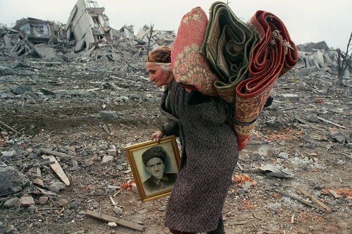 An Old Woman Leaving Her Home With Just A Portrait Of Her Husband And Rugs. Russian Soldiers Gave Her Just 5 Minutes To Pack Her Bags And Leave Before They Destroyed Her Home And Everything In It. Her Sons And Husband Were Already Dead. She Had Lost Everything. May 1995, Grozny 