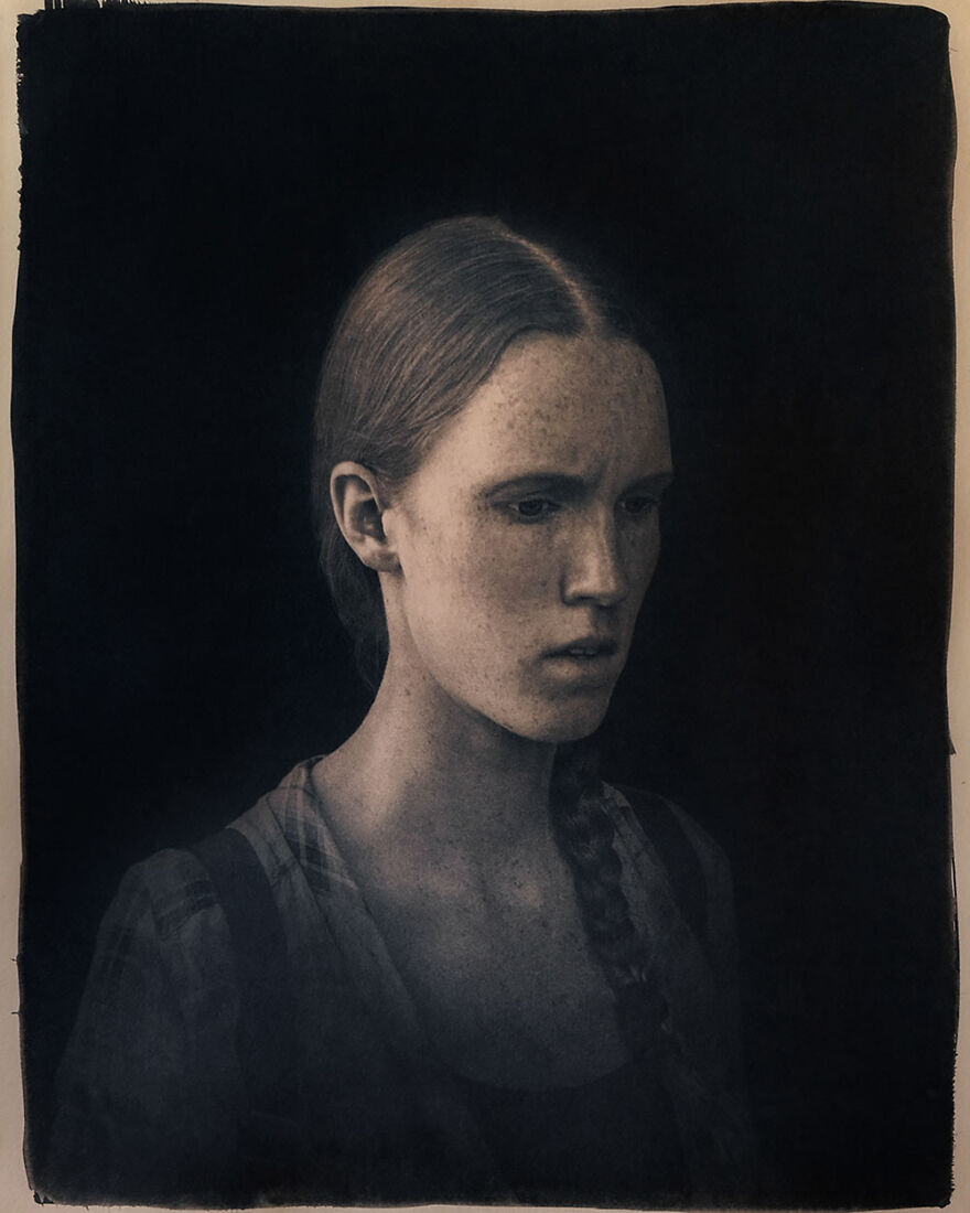 Portrait of a beautiful woman with red hair and freckles in a dark setting, captured by photographers around the world.