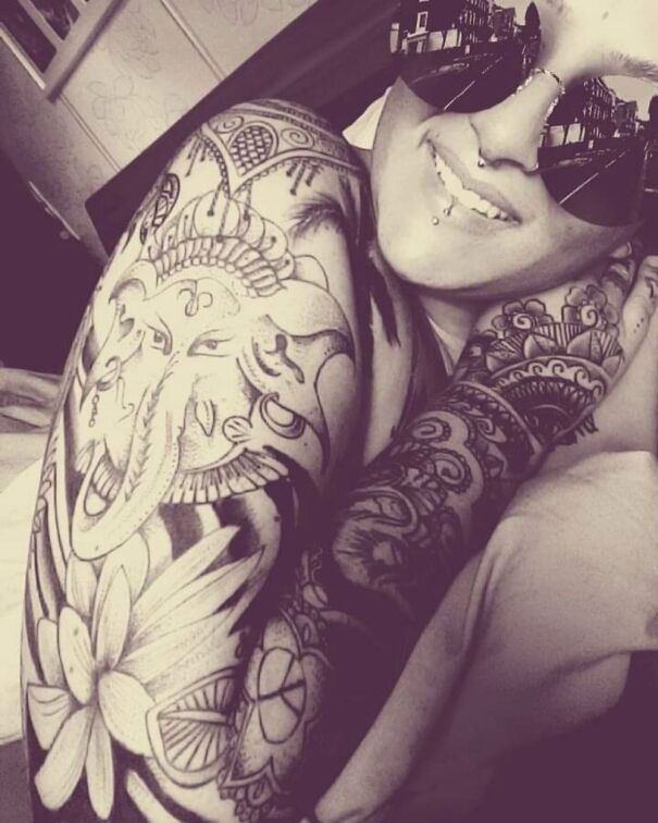 Person displaying impressive new tattoo featuring intricate designs on the arm, smiling while wearing sunglasses.