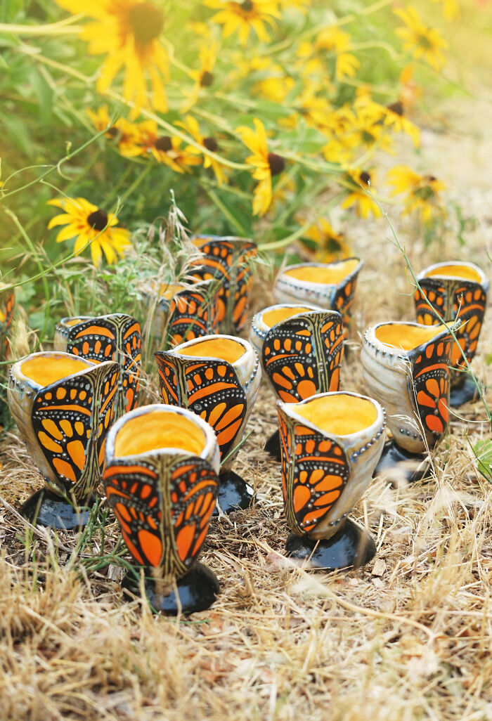 Nature-inspired ceramic cups with butterfly patterns in a garden setting.