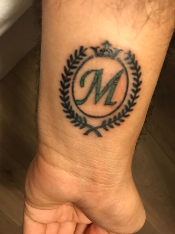 "Impressive new tattoo featuring a green 'M' with laurel wreath and crown on a wrist."