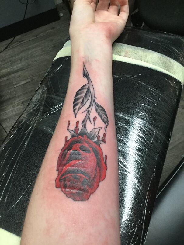 New tattoo of a red rose with leaves on a forearm, showcasing impressive artistic detail and style.