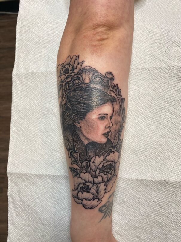A realistic portrait tattoo with floral details on an arm, showcasing impressive new artwork.
