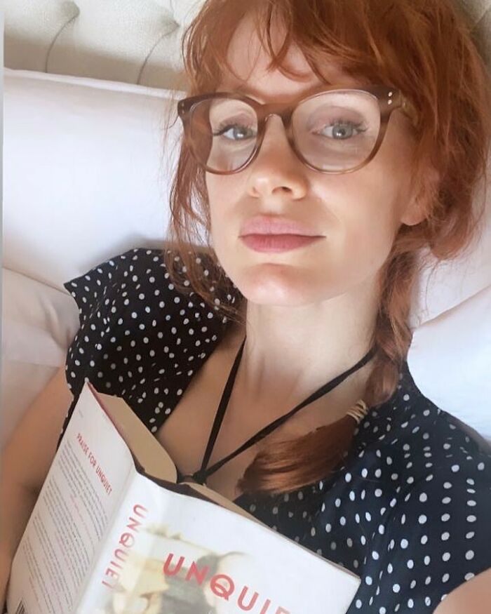 Red-haired woman with glasses reading a book lying on a bed about actors not being well-connected or rich. Red-haired woman with glasses reading a book lying on a bed about actors not being well-connected or rich.