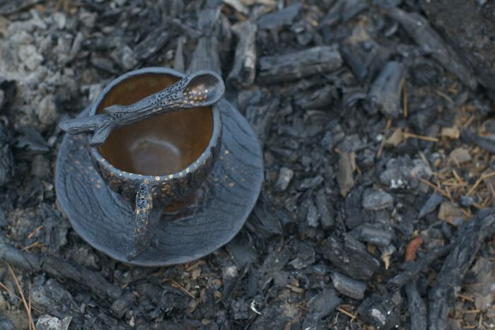 Nature-inspired ceramic cup and saucer with a spoon resting on top, set against a backdrop of dark, textured bark.