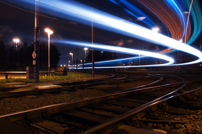 Long exposure shot of a tram at night, creating ethereal light trails over train tracks.