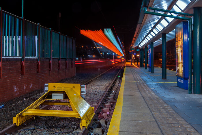 Long exposure shot of a tram station at night, creating a surreal, otherworldly effect with vibrant light trails.