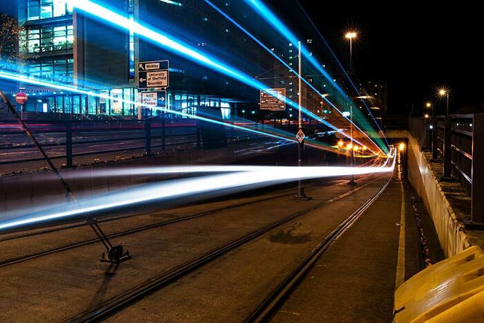 Long exposure photo of trams at night, creating streaks of light and a futuristic atmosphere.
