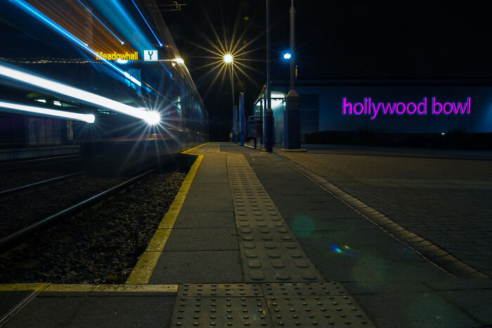 Long exposure image of a tram at night, emitting bright light trails, with "hollywood bowl" sign in the background.