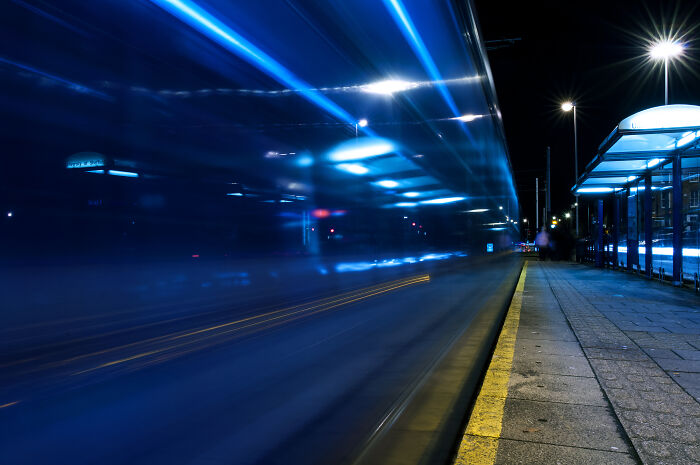 Long exposure shot of a tram at night, creating a futuristic and otherworldly visual effect on a city street.