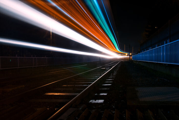 Long exposure of trams at night, creating surreal light trails across railway tracks.