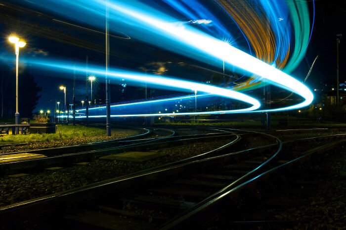 Long exposure of tram lines at night, creating ethereal, otherworldly light trails across the dark railway tracks.