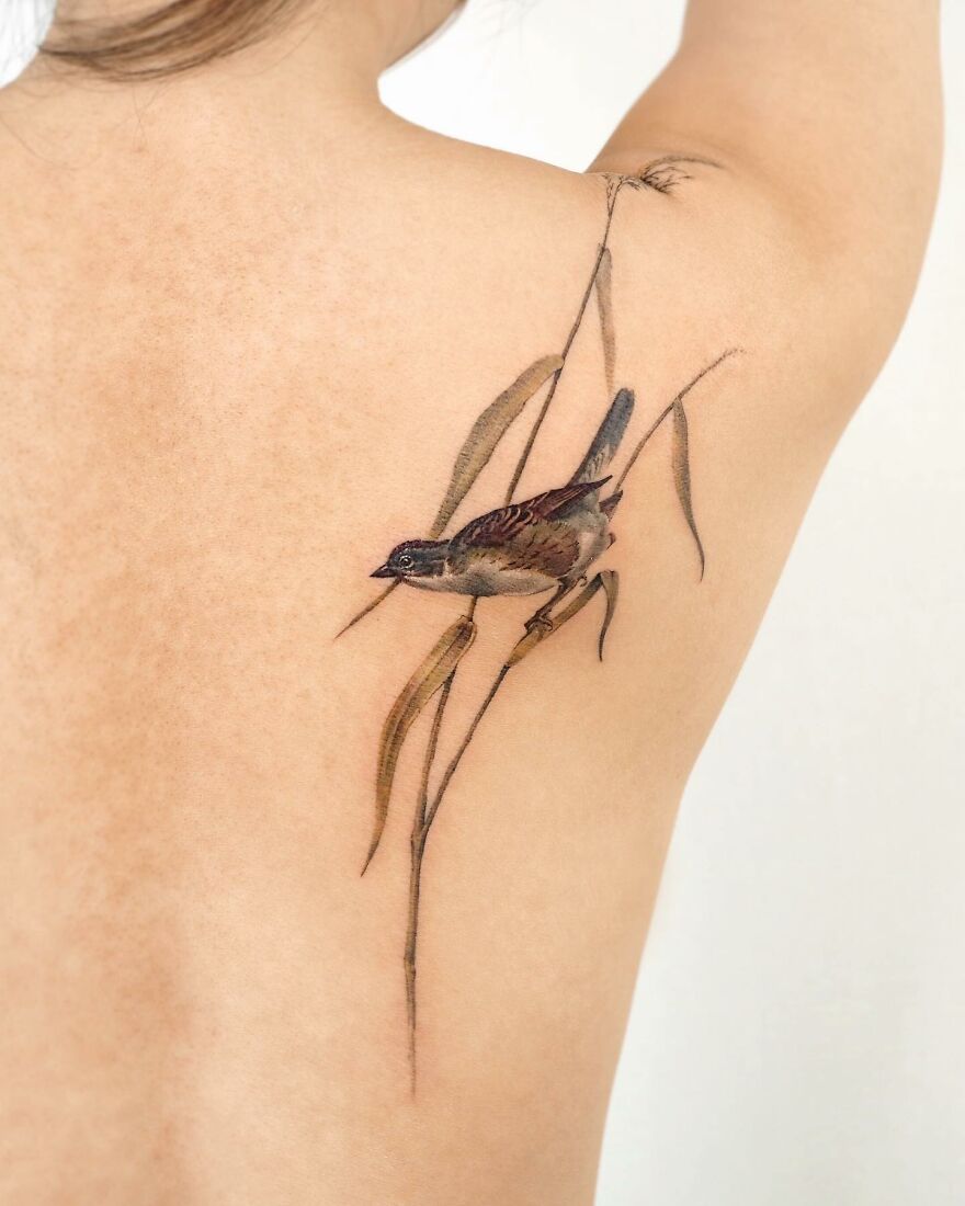 Painting-like tattoo of a bird on a woman's back, showcasing detailed artistry.