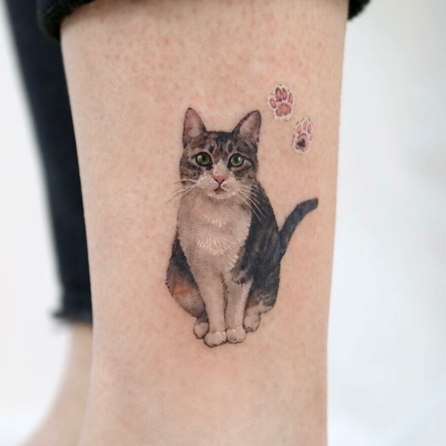 Cat tattoo with painting-like detail on skin, featuring realistic fur and paw prints.