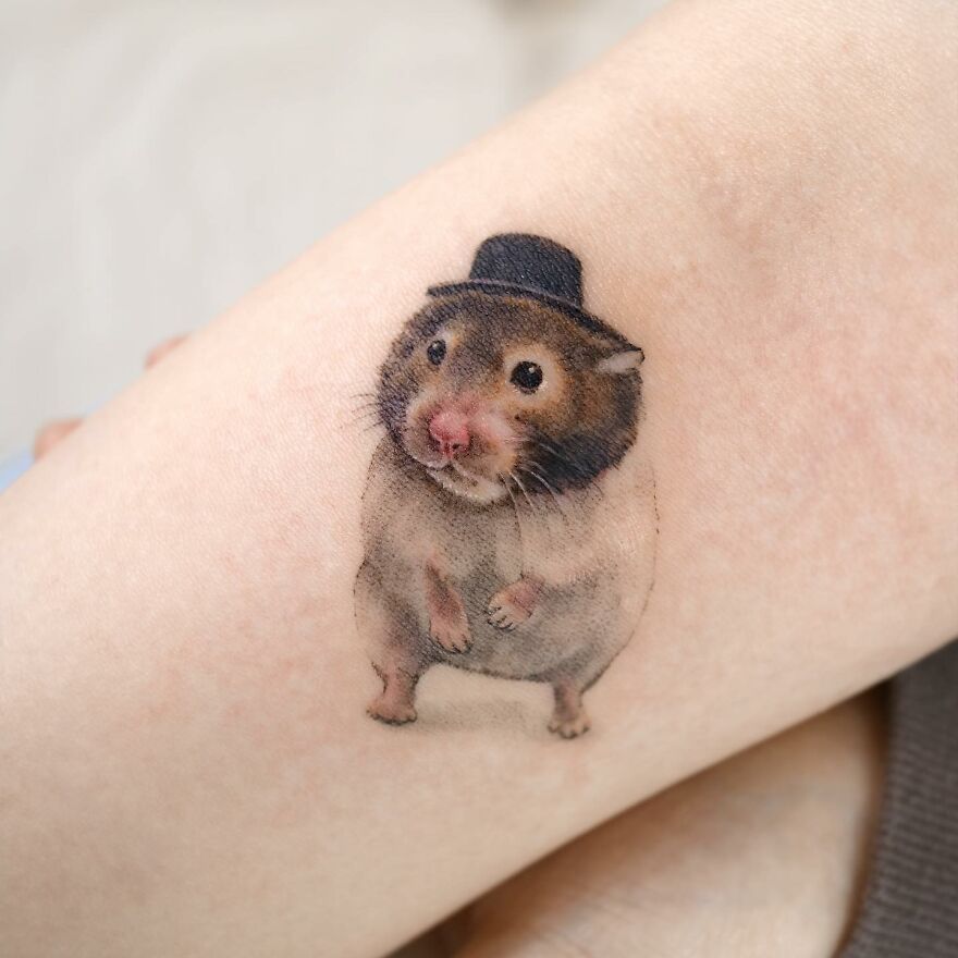 Tattoo of a hamster with a top hat, showcasing painting-like detail on skin.